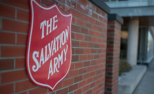 Red Salvation Army shield sign mounted on the exterior brick wall of the Salvation Army building.
